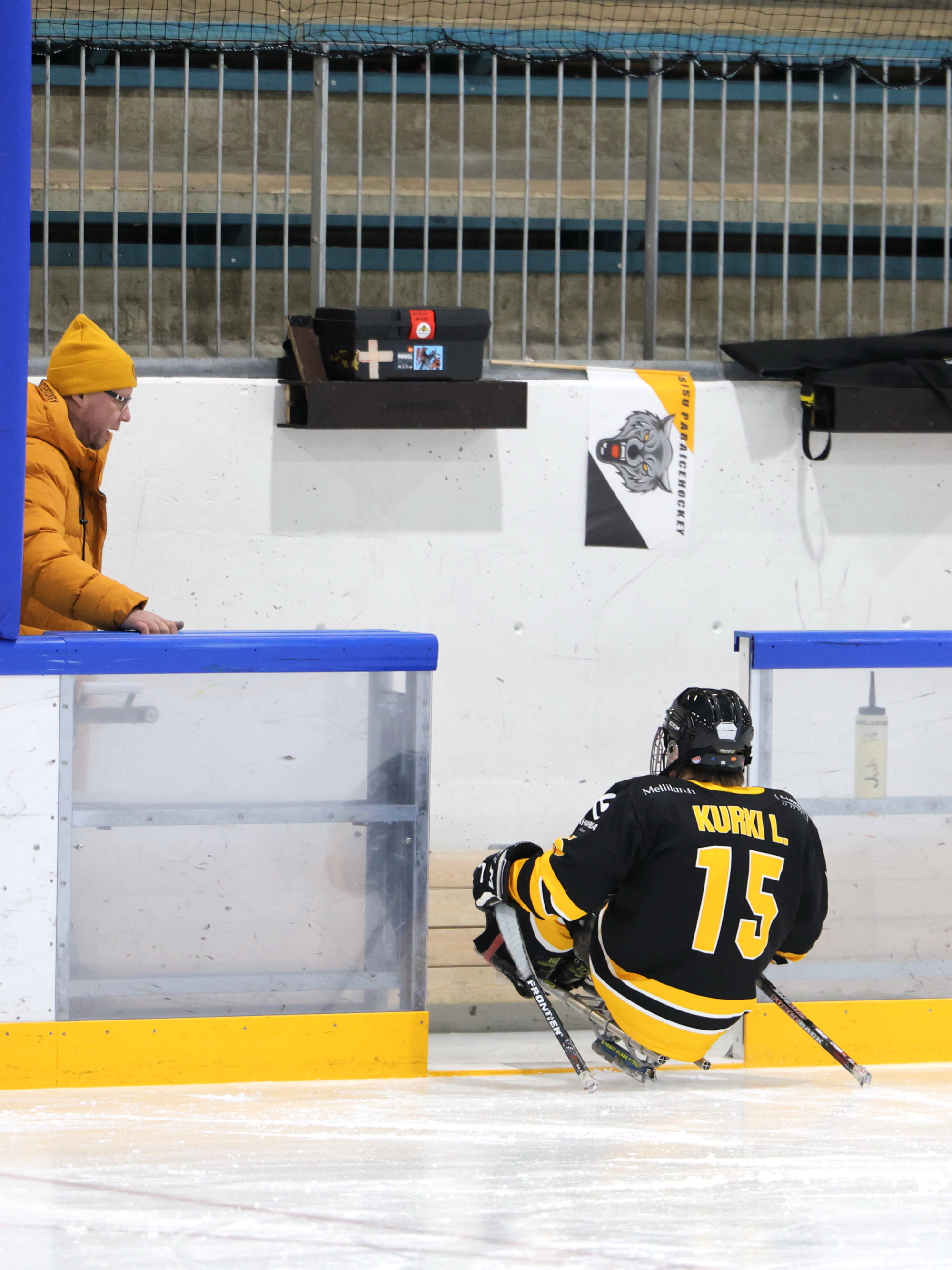 Kuvassa parajääkiekkoilija menee vaihtoaitioon jäältä avoimesta kaukalon luukusta.